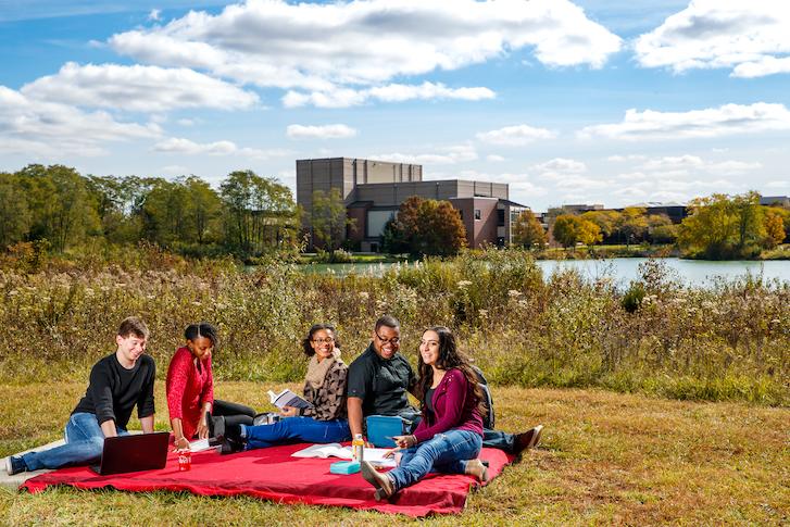 Students sitting on blanket outside of campus by pond