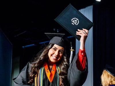 Graduate holding up degree on stage during Commencement ceremony